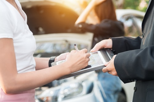 mujer y agente de seguros examinando el coche tras un accidente