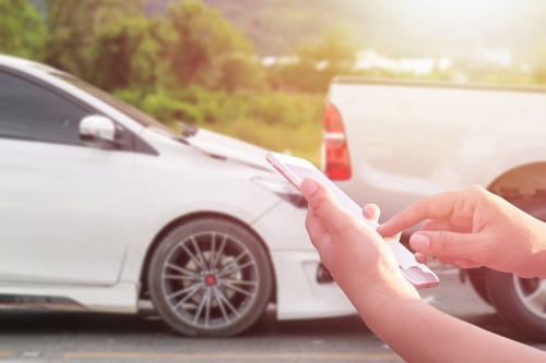 Mano de una mujer utilizando un smartphone en la carretera tras un accidente de tráfico