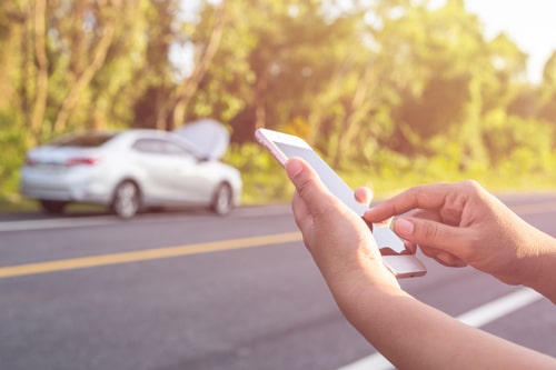 Mano de mujer usando smartphone y desenfoque de su coche roto aparcando