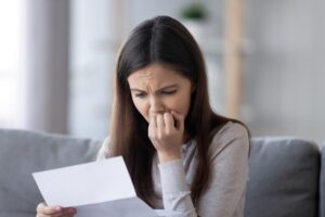 Young woman feeling stressed and upset while reading bad news in a paper mail letter, concerned about financial issues or academic struggles.