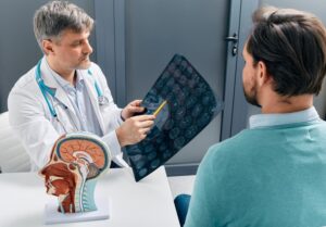 Physician discussing MRI brain scan results with male patient, providing diagnosis for diseases and head injuries.