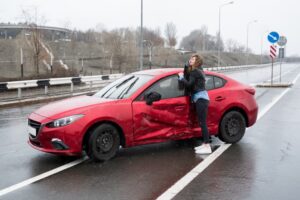 Woman beside damaged car post-accident, seeking assistance and contacting car insurance.