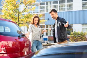 Young man and woman having a dispute after a car accident on a street outdoors.