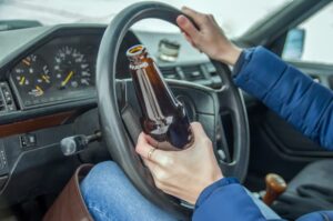 Drunk girl drives a car with a bottle of alcohol in her hand