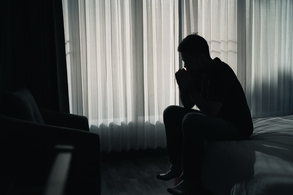depressed man sadly sitting on the bed in the bedroom