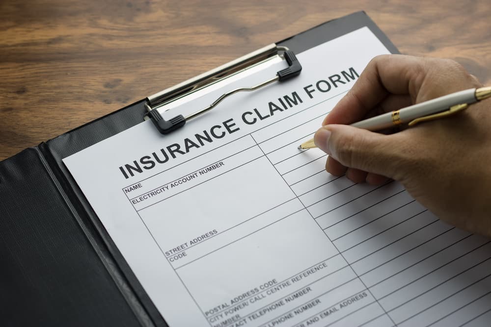 Hand holding a pen, filling out an application form for registering a health insurance claim.